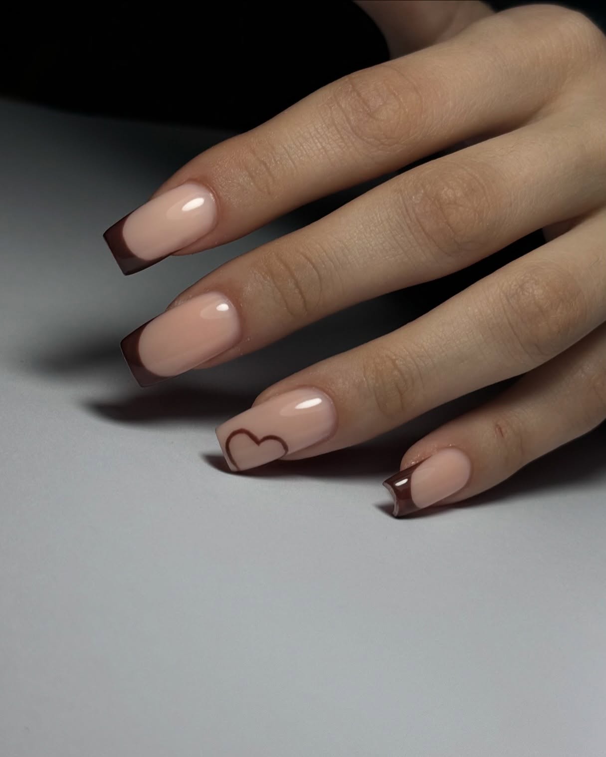 Nude French manicure with a delicate brown heart accent on the ring finger